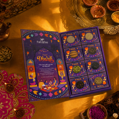 An open Palm Tree Diwali gift box displayed on a warm golden surface, surrounded by decorative lamps, spices, and traditional ornaments. The purple box is open to show the illustrated left panel with 'Happy Diwali' text and the right panel containing eight small sachets labeled with flavors such as Almond, Peanut Butter, and Chocolate.